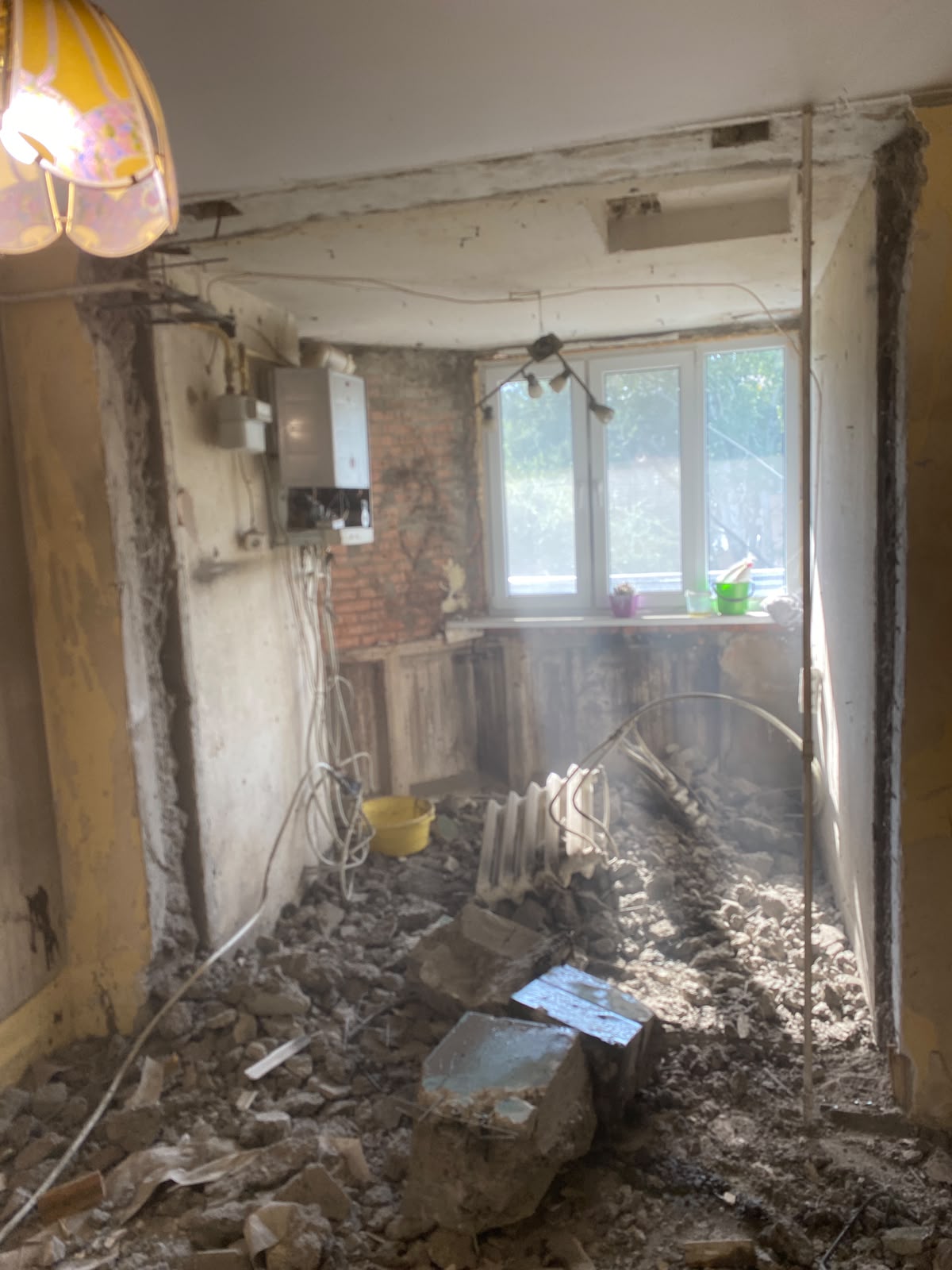 Perete demolat într-un apartament, cu moloz și un calorifer pe podea