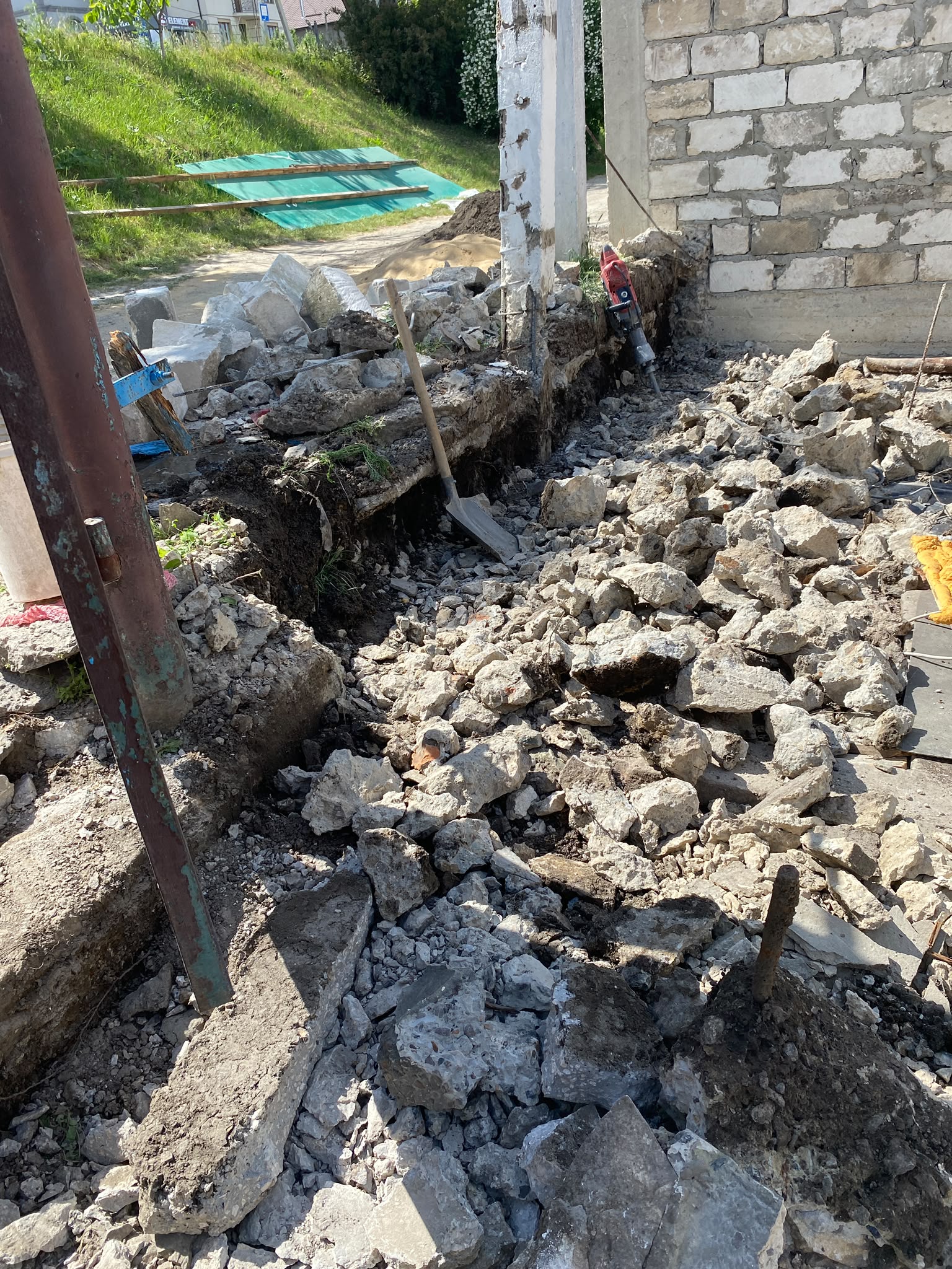 Fundație spartă cu ciocanul demolator și șanț săpat lângă un zid de piatră