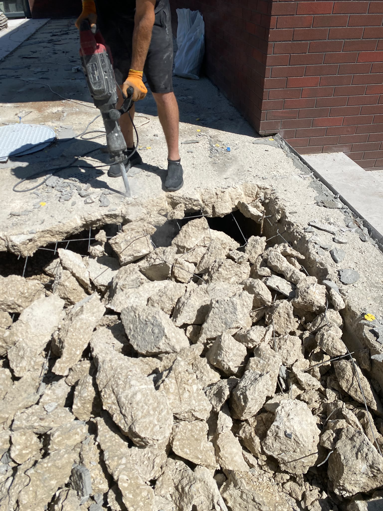 Muncitor sparge o placă de beton cu ciocan demolator lângă o clădire din cărămidă
